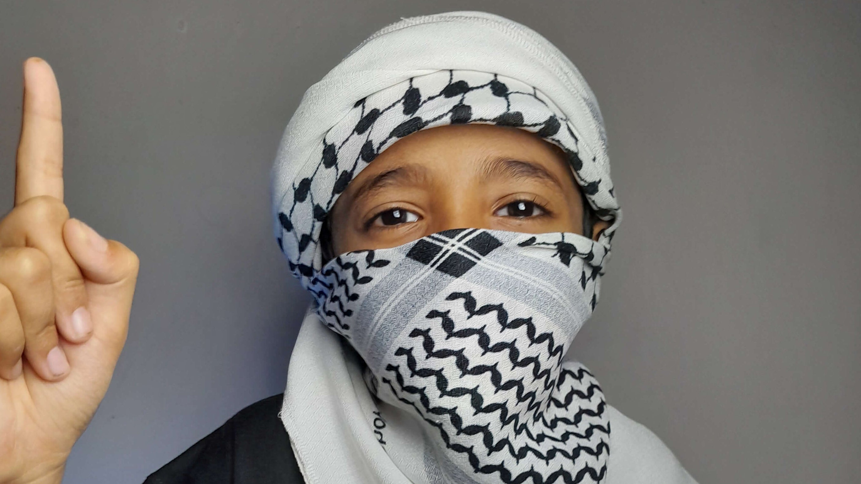 Person wearing a headscarf and black t-shirt with a graphic design, making a peace sign.